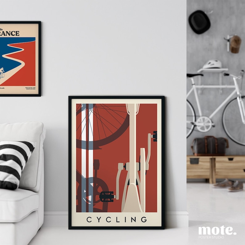 May include: A framed poster with a cycling theme. The artwork features a bicycle illustration in cream and red, with the word "CYCLING" at the bottom. Another framed poster is visible on the left. The room has a white sofa and a bicycle.
