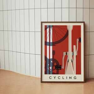 May include: Framed art print featuring a minimalist bicycle design in red, white, and blue. The word "CYCLING" is printed in a sans-serif font at the bottom. The artwork is displayed against a white tiled wall.