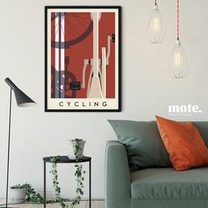 May include: A framed poster with a cycling theme. The artwork features a bicycle illustration in cream, red, and blue tones, with the word "CYCLING" at the bottom. The poster is displayed above a small black side table and a green sofa.