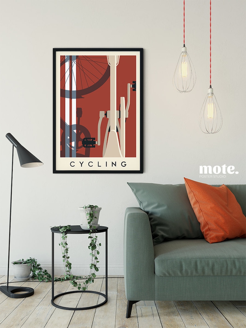 May include: A framed poster with a cycling theme. The artwork features a bicycle illustration in cream, red, and blue tones, with the word "CYCLING" at the bottom. The poster is displayed above a small black side table and a green sofa.