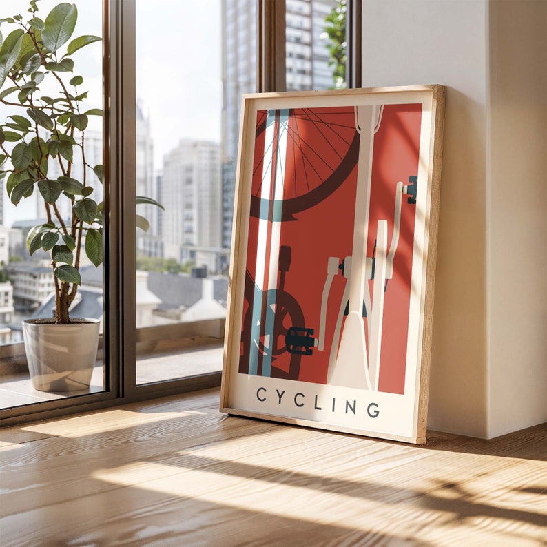 May include: A framed poster with a cycling theme. The artwork features a bicycle wheel, frame, and pedals in white, blue, and black against a red background. The word "CYCLING" is printed in white at the bottom. The frame is made of light-colored wood.