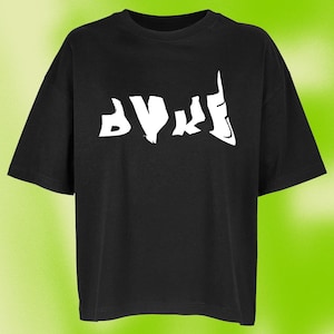 Könnte beinhalten: Ein schwarzes T-Shirt mit kurzen Ärmeln und einem weißen Grafikdruck auf der Brust. Das Design besteht aus stilisierten, gezackten weißen Buchstaben, die wie ein Logo oder abstrakter Text aussehen. Das T-Shirt hat einen Rundhalsausschnitt und eine lockere Passform.