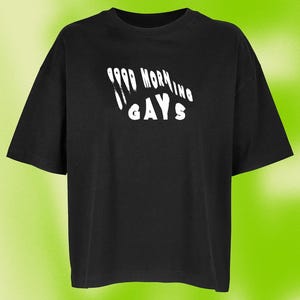 Könnte beinhalten: Ein schwarzes T-Shirt mit kurzen Ärmeln und weißem Text auf der Brust, der GOOD MORNING GAYS lautet. Die Schrift hat einen tropfenden Farbeffekt, wobei die Worte GOOD MORNING über dem Wort GAYS in einer fetten, serifenlosen Schrift gebogen sind.