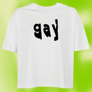 Könnte beinhalten: Ein weißes T-Shirt mit kurzen Ärmeln und dem Wort "gay", das in einer fetten, schwarzen, handgezeichneten Schriftart auf der Brust gedruckt ist. Das Kleidungsstück hat einen Rundhalsausschnitt, eine lockere Passform und gerade Säume.