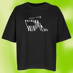 Könnte beinhalten: Ein schwarzes T-Shirt mit kurzen Ärmeln und weißem Text auf der Brust, der EAT THE PATRIARCHY lautet. Das Wort PATRIARCHY ist mit länglichen vertikalen Buchstaben gestaltet, während die Wörter EAT THE in einer kleineren Standardschrift darüber stehen.