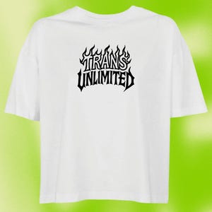 Könnte beinhalten: Weißes T-Shirt mit dem schwarzen Schriftzug "TRANS UNLIMITED" in einer flammenden Schriftart. Das Shirt hat kurze Ärmel und einen Rundhalsausschnitt. Der Hintergrund ist ein grüner und gelber Farbverlauf.