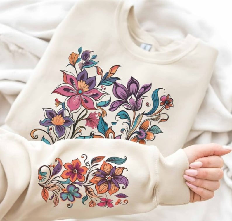 Puede incluir: Una sudadera de color crema con un dise&ntilde;o floral. El dise&ntilde;o presenta una variedad de flores en tonos de rosa, morado, naranja y azul. Las flores est&aacute;n dispuestas en un racimo en la parte delantera de la sudadera y en la manga.