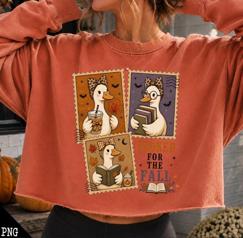 May include: A rust-colored crewneck sweatshirt featuring three stamp-style illustrations of ducks wearing leopard-print headbands. The ducks are depicted holding a coffee cup, a stack of books, and an open book. The text reads BOOKS FOR THE FALL.
