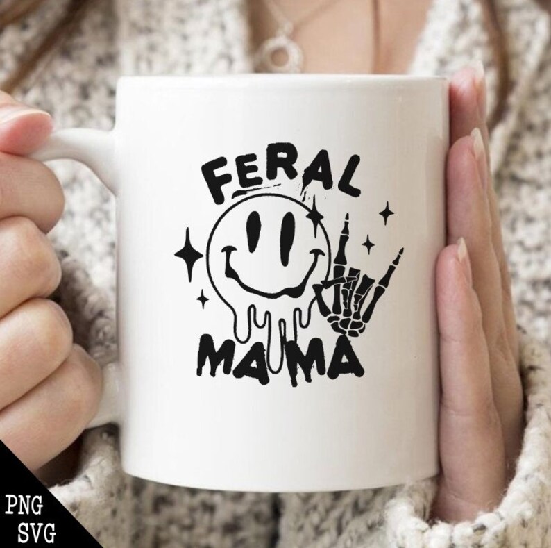 Pu&ograve; includere: Tazza in ceramica bianca con un design grafico nero. Il design presenta un viso sorridente che cola con una mano scheletrica che fa il segno 'rock on'. Il testo 'Feral Mama' &egrave; sotto il design.