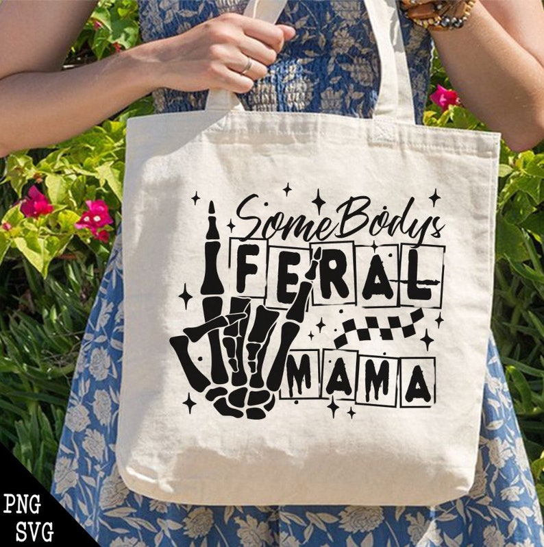 Pu&ograve; includere: Una borsa tote bianca con testo nero che recita "Some Body's Feral Mama" con una mano scheletrica che fa un gesto rock and roll.