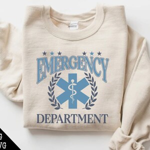 May include: A beige sweatshirt with a blue and white graphic design that says "Emergency Department" with a star of life symbol.