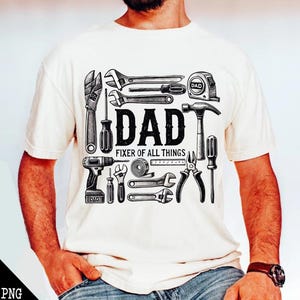 May include: Cream-colored t-shirt featuring a collection of tools, including wrenches, a hammer, and a drill. The text "DAD FIXER OF ALL THINGS" is prominently displayed in the center. The design is in black and white.