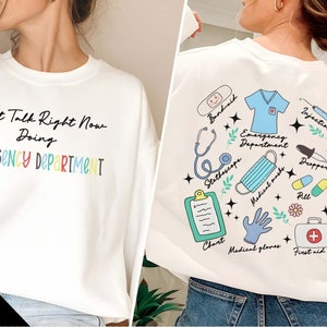 May include: White sweatshirt with the text "Can't Talk Right Now Doing EMERGENCY DEPARTMENT" in rainbow colors. The back of the sweatshirt has a white background with colorful illustrations of medical supplies, including a stethoscope, bandaid, chart, medical gloves, first aid kit, medical mask, dropper, pill, and injection.