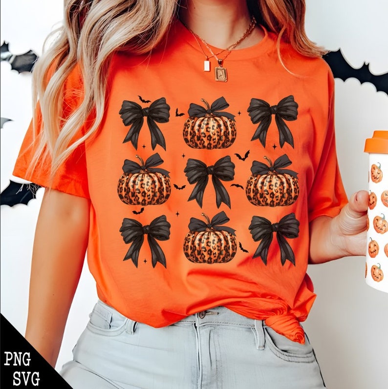 May include: Orange t-shirt featuring a repeating pattern of leopard print pumpkins with black bows and small bat silhouettes. The shirt is a short-sleeved crew neck and is made of a soft material. The design is perfect for Halloween.