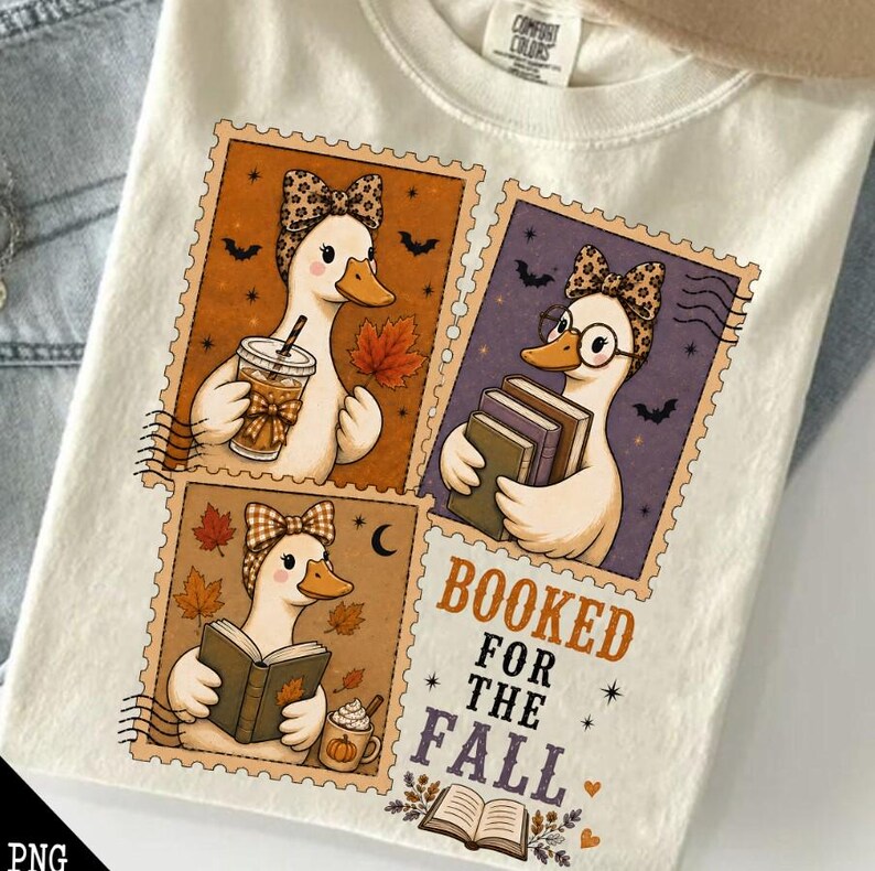 May include: A cream-colored t-shirt featuring three stamp-style illustrations of ducks wearing patterned bows. The ducks are depicted holding a coffee cup, a stack of books, and an open book, surrounded by autumn leaves, bats, and the text BOOKED FOR THE FALL.