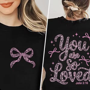 May include: Black t-shirt with a pink lace bow on the front and the text "You are so loved John 3:16" on the back in a pink lace font.