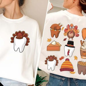 Peut inclure: Sweat-shirt blanc avec un motif de dent sur le thème de Thanksgiving sur le devant. Le dos du sweat-shirt présente plusieurs motifs de dents sur le thème de Thanksgiving, dont une dinde, une citrouille, une tarte et une tasse de café.