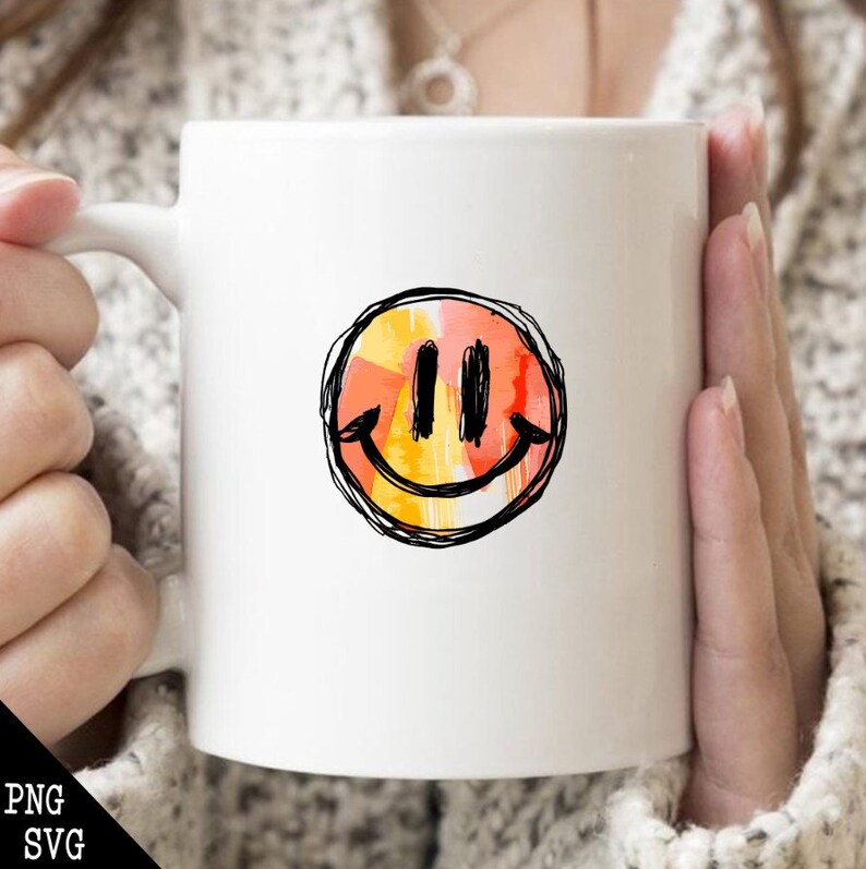 May include: White ceramic mug with a hand-drawn smiley face in orange, yellow, and red colors. The smiley face is outlined in black.