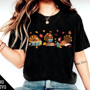 May include: A black t-shirt with a graphic of three turkeys reading books. The turkeys are surrounded by fall leaves.