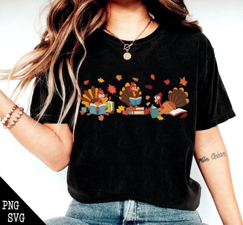 May include: A black t-shirt with a graphic of three turkeys reading books. The turkeys are surrounded by fall leaves.