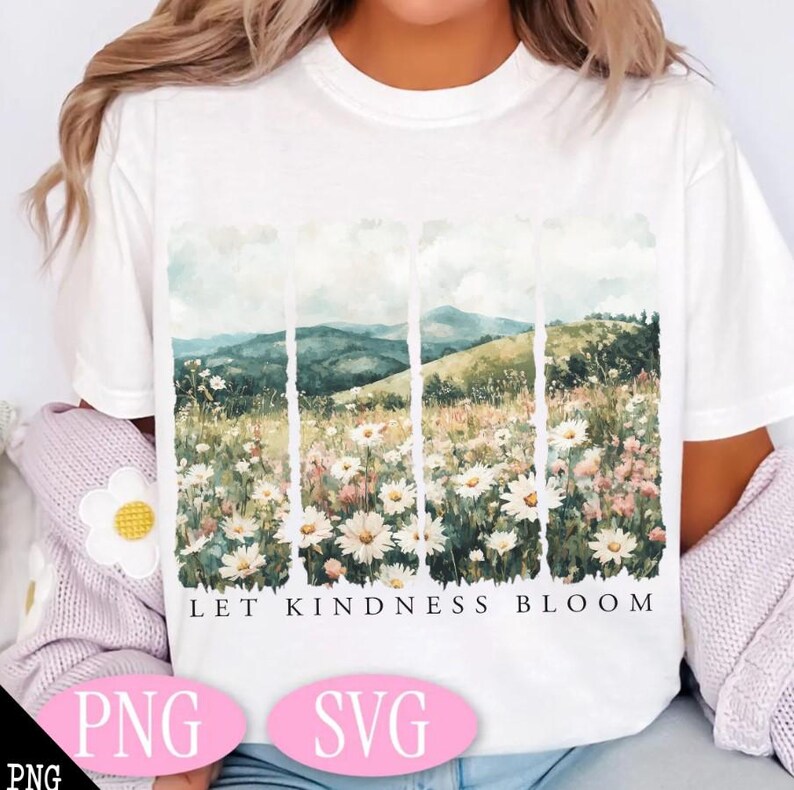 Op de afbeelding: Wit T-shirt met een aquarelontwerp van een bloemenveld en glooiende heuvels. De tekst "Let Kindness Bloom" is onder de afbeelding gedrukt.