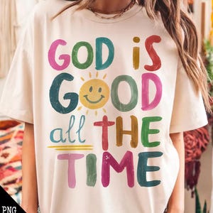 Könnte beinhalten: Ein weißes T-Shirt mit einem bunten Grafikdesign, auf dem "Gott ist gut die ganze Zeit" steht. Die Grafik zeigt eine lächelnde Sonne mit einem gelben Gesicht und einem roten Kreuz.