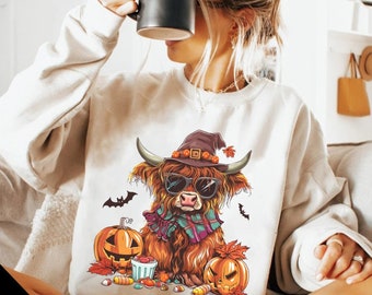 May include: Cream-colored sweatshirt featuring a Halloween-themed graphic. The graphic includes a Highland cow wearing sunglasses, a witch hat, and a scarf, with pumpkins, bats, and candy corn. The sweatshirt is a cozy, seasonal apparel item.