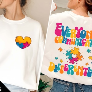 May include: White sweatshirt with a colorful puzzle piece heart on the front and the text "Everyone Communicates Differently" in a retro font on the back.