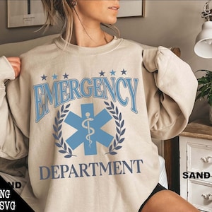 May include: A beige sweatshirt with a blue and white graphic print that says "EMERGENCY DEPARTMENT" with a star of life symbol and laurel wreath.