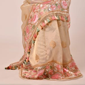 Pode incluir: Len&ccedil;o bege transparente com bordados florais em rosa, verde e dourado. O len&ccedil;o apresenta uma borda decorativa e borlas em tons de rosa, verde e p&ecirc;ssego. O len&ccedil;o est&aacute; drapeado, mostrando seu tecido delicado e design.