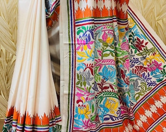 May include: Ivory-colored sari with intricate floral and geometric embroidery in vibrant colors. The border features orange and white patterns, with accents of blue, green, and red. The sari is draped, showcasing the detailed craftsmanship.
