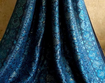 Può includere: Un tessuto blu profondo caratterizzato da un intricato motivo floreale e paisley ripetuto in tonalità turchese, blu navy e oro metallizzato. Il tessuto presenta un design fitto con un bordo prominente e un'etichetta quadrata blu con la scritta RBC.