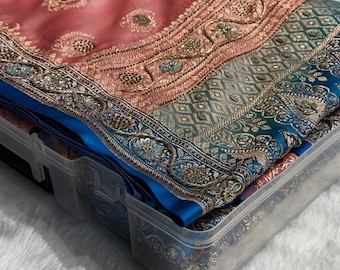 May include: A folded coral pink fabric featuring gold embroidered paisley motifs and a wide border with intricate teal and gold geometric patterns, metallic floral embroidery, and decorative beadwork, all contained within a clear plastic storage box.