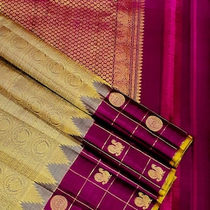 May include: A luxurious silk sari in shades of gold, silver, and magenta. The sari features intricate woven patterns, including circular motifs and peacock designs. The border is a deep magenta with gold accents.
