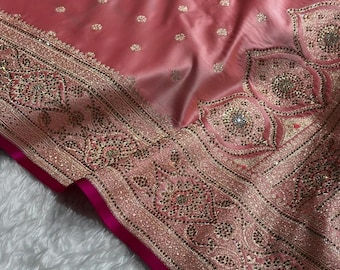 May include: A dusty rose satin fabric featuring a wide, ornate border with intricate gold embroidery, small metallic beads, and reflective sequins. The main body of the fabric is decorated with a repeating pattern of small, scattered gold floral motifs.