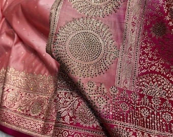 May include: A luxurious pink saree with intricate gold embroidery and embellishments. The fabric has a shimmering, satin-like finish, with detailed floral and geometric patterns along the borders and central design. The saree features a rich, vibrant color palette.