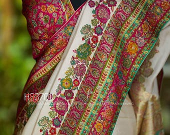 May include: Ivory sari with detailed floral embroidery in pink, green, yellow, and blue. The sari has a detailed border and a matching blouse with a floral pattern. The text "HB3701" is visible.