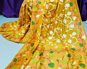 May include: A yellow saree with a white floral pattern and green and pink accents. The saree has a white border with a delicate lace trim.