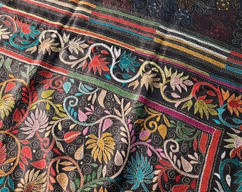 May include: Black fabric with colorful embroidery of floral patterns. The embroidery is done in a variety of colors, including red, green, blue, yellow, and pink. The fabric has a textured surface and is likely made of silk.