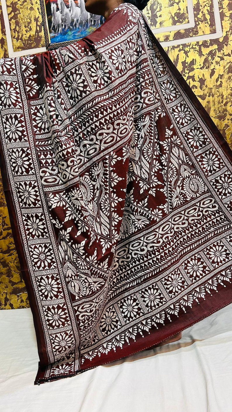 May include: A maroon textile with a white floral and geometric pattern. The fabric is draped, showcasing the intricate design. The pattern includes stylized flowers, leaves, and geometric shapes, creating a detailed and ornate appearance. The textile has a border with a repeating floral design.