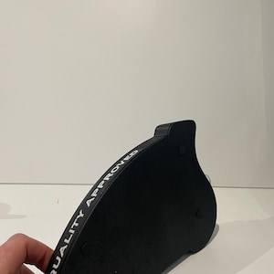 May include: A black, curved object with the text "QUALITY APPROVED" in white lettering. The object has a rounded shape with a small, raised section on one end and three small, circular feet on the bottom.