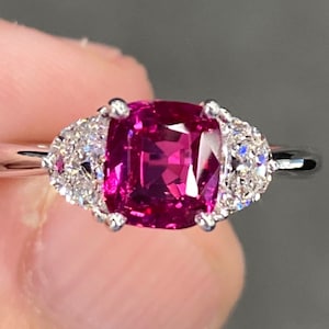 May include: A pink gemstone ring with two smaller diamond accents on either side of the center stone. The ring is set in white gold.