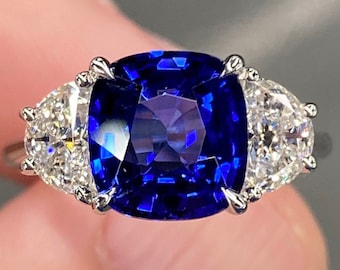 May include: A ring with a large, cushion-cut sapphire surrounded by two smaller, pear-shaped diamonds.