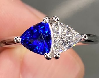 May include: A silver ring with a blue sapphire and a white diamond set in a triangular shape.