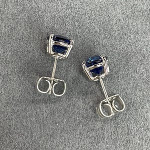 Pode incluir: Um par de brincos de prata com pedras preciosas quadradas azuis escuras. Os brincos t&ecirc;m um design simples e elegante, com as pedras preciosas embutidas em uma configura&ccedil;&atilde;o de quatro garras. As hastes dos brincos t&ecirc;m fechos de borboleta.