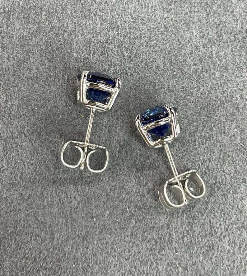 Pode incluir: Um par de brincos de prata com pedras preciosas quadradas azuis escuras. Os brincos t&ecirc;m um design simples e elegante, com as pedras preciosas embutidas em uma configura&ccedil;&atilde;o de quatro garras. As hastes dos brincos t&ecirc;m fechos de borboleta.