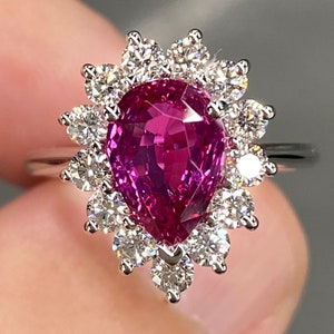 May include: A pear-shaped pink sapphire ring with a halo of diamonds. The ring is set in white gold.