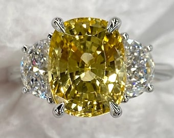 May include: A three-stone ring with a large, cushion-cut yellow gemstone and two smaller, oval-cut white gemstones. The ring has a silver band and prongs securing the stones.