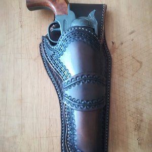 Könnte beinhalten: Ein braunes Lederholster mit aufwendigen Nähten und einer Waffe darin.