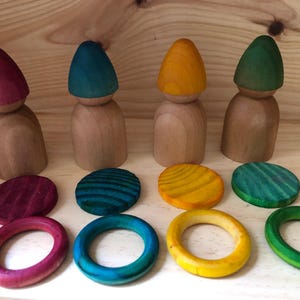 Peut inclure: Ensemble de jouets en bois comprenant quatre poup&eacute;es en bois avec des chapeaux coniques color&eacute;s en rouge, bleu sarcelle, jaune et vert. L'ensemble comprend des disques et des anneaux en bois de couleur assortie.